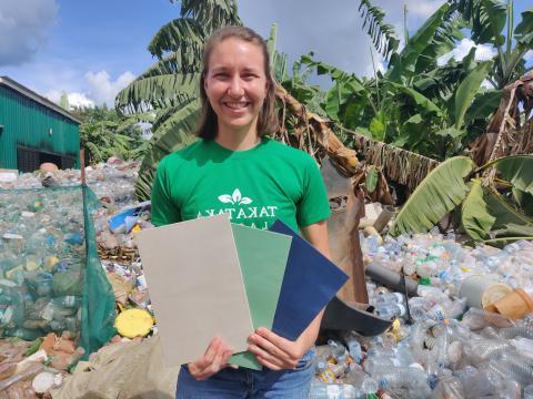 Paige outside st和ing in front of piles of plastic, holding a recycled plastic product