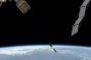 Tiny satellite floats above Earth in between much larger space science equipment.